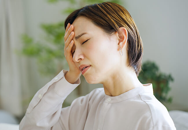 頭痛で頭を右手でおさえる女性